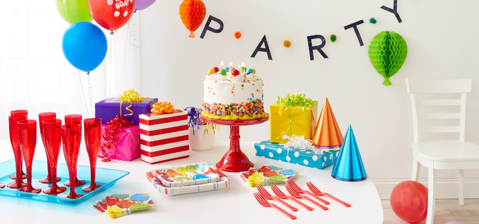 Une organisation de fête colorée, dont une bannière qui se lit : « fête », un bouquet de ballons et une table agrémentée d’un gâteau, de cadeaux, de chapeaux de fête et de vaisselle colorée.