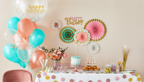 Une décoration murale de bon anniversaire est suspendue au- dessus d’une table avec gâteau et gâteries. Un bouquet de ballons flotte à gauche de la table.