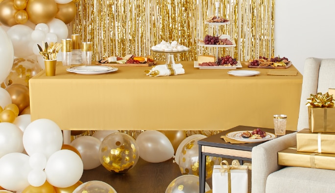 Party display setting atop a gold table cover surrounded by white and gold balloons.