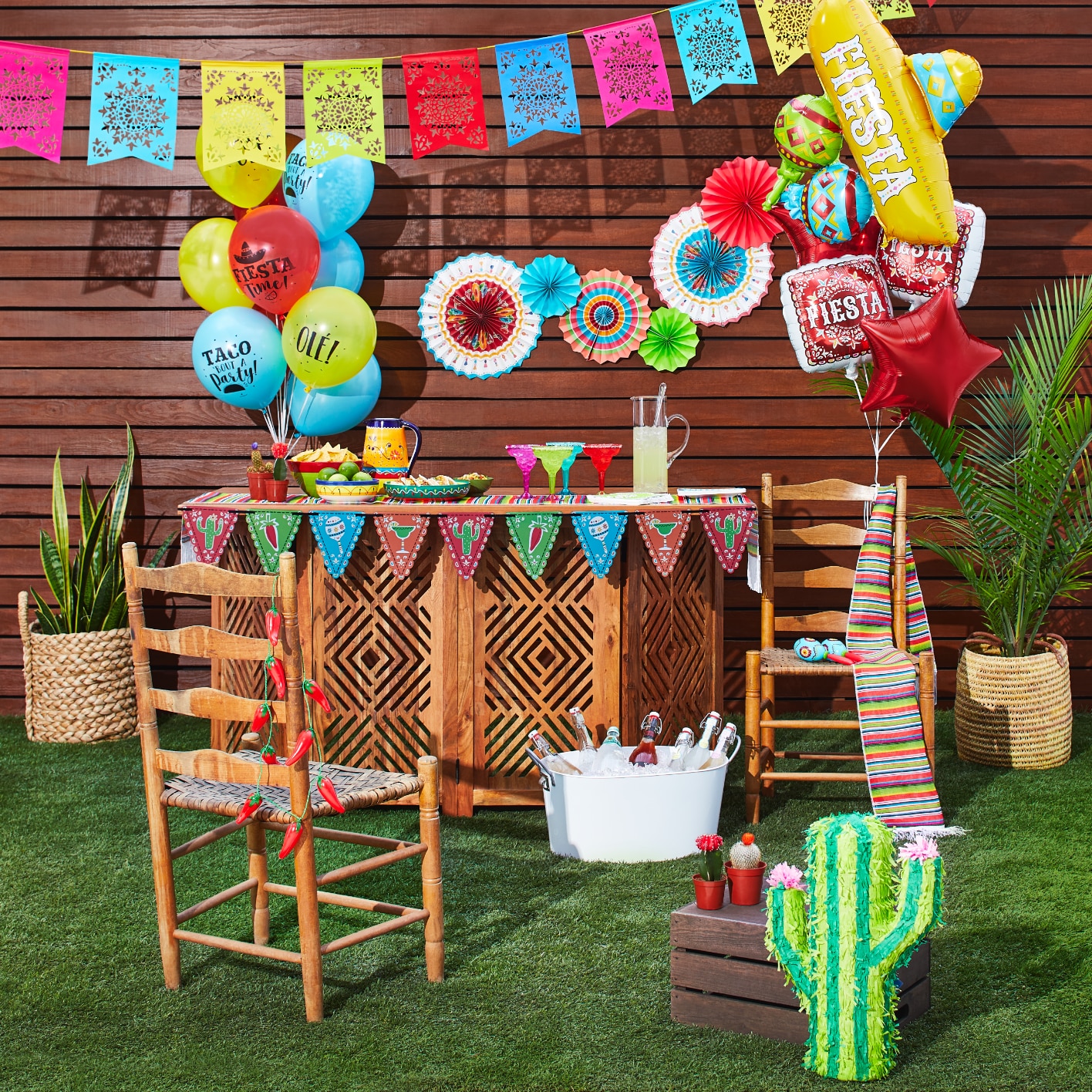 Une fête extérieure décorée de ballons multicolores à thème de fiesta, d’éventails en papier, de bannières à fanions et d’une pinata en forme de cactus.