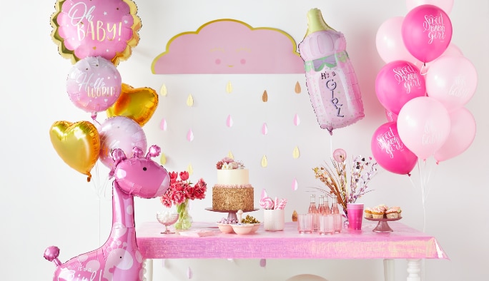 A room styled with white, pink, and gold baby-themed balloons and décor including an “It's a Girl” wild safari giraffe foil balloon.