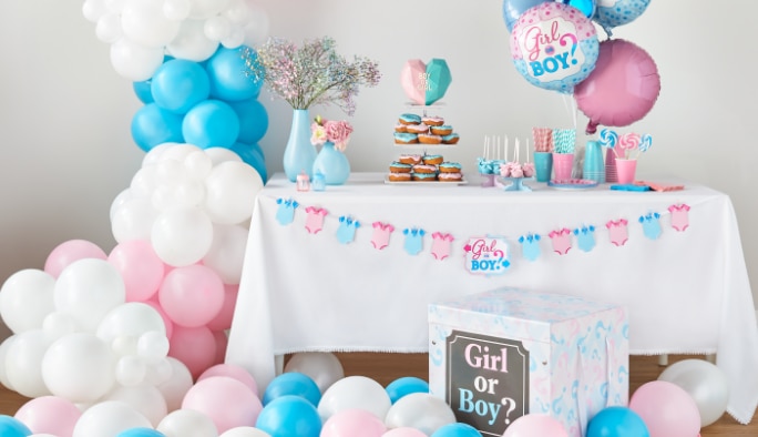 A treat table decorated with “Girl or Boy?” themed party supplies and white, pink and blue balloons. 