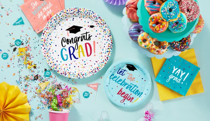 Une table remplie de vaisselle à thème « Congrats Grad » pour les finissants, de desserts et de confettis colorés.