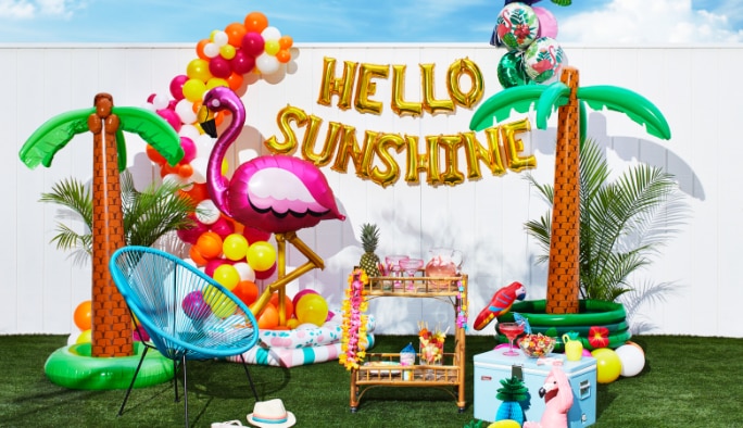 Une cour décorée avec une guirlande de ballons dorés « Hello Sunshine », un ballon en aluminium Airwalker en forme de flamant rose et d’autres accessoires colorés.