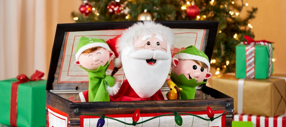 Two toy elves and a toy Santa in a box with Christmas presents