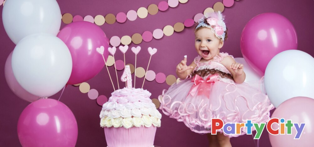 A little girl celebrates her 1st birthday with a fluffy dress, pink balloon decorations, pink circle dot streamers from Party City and a cupcake cake.