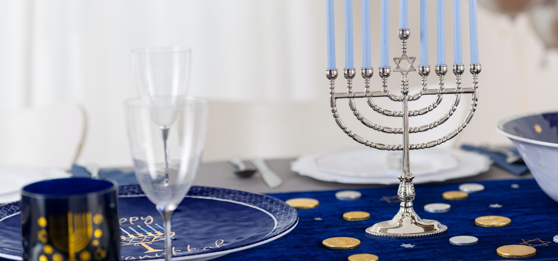 A table styled with a navy-blue Hanukkah joy table runner, a silver menorah and other blue, silver and gold dinnerware and accessories.