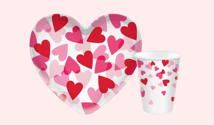 A Valentine's Day heart-shaped plastic bowl and a Valentine's Day Cross My Heart cup. Both items are white with pink and red heart prints. 