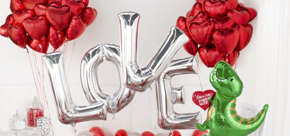 A room decorated with silver L-O-V-E letter foil balloons, a cluster of red heart foil balloons, a You’re Dino-Mite dinosaur-themed balloon.