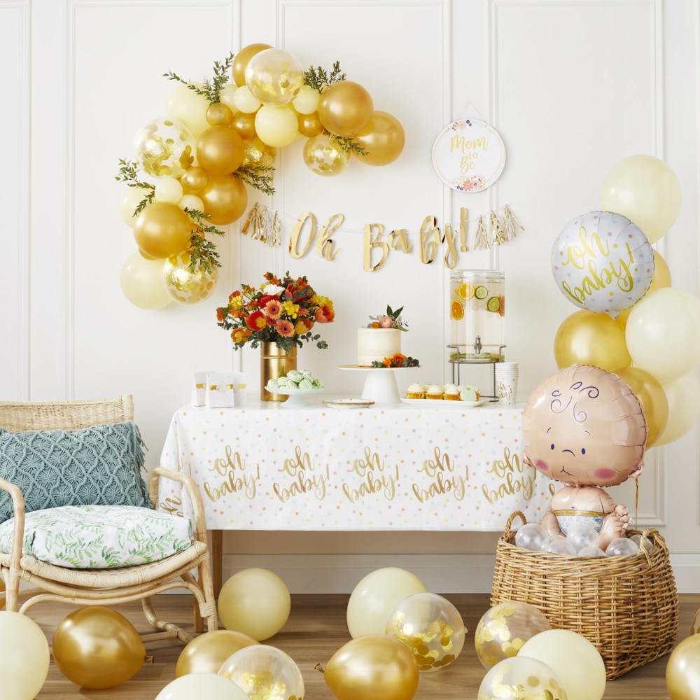 Une table entourée de ballons en latex dorés et jaunes, d'un ballon en aluminium en forme de bébé et de décorations à thème « Oh Baby ».