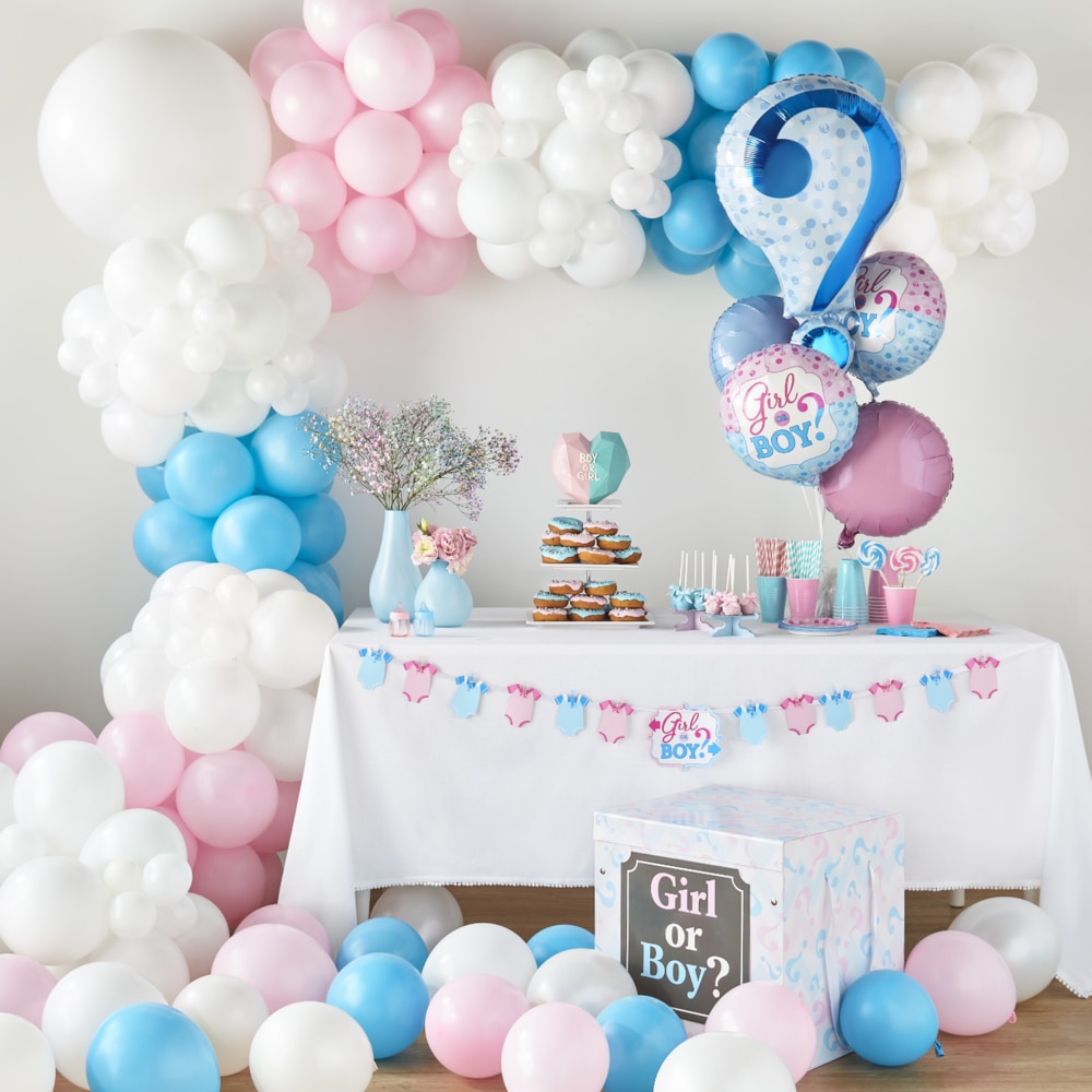 A dessert table filled with white, pink and blue “Girl or Boy?” themed party supplies and surrounded by matching latex and foil balloons. 