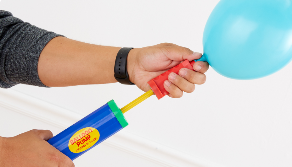 A close-up view of an adult’s hands inflating a blue latex balloon with a blue, yellow, red and green balloon pump.