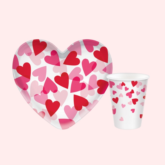 A Valentine's Day heart-shaped plastic bowl and a matching cup, both white with a red and pink heart print.