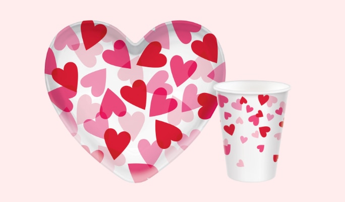 A Valentine's Day heart-shaped plastic bowl and a matching cup, both white with a red and pink heart print.