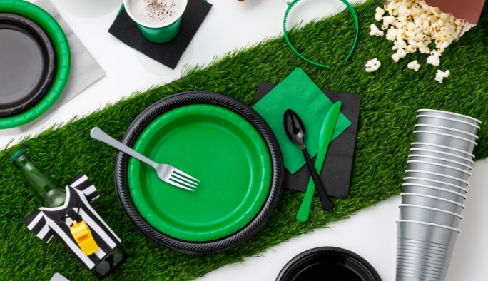 Une table avec de la vaisselle verte et noire et des accessoires à thème sportif, y compris une housse pour bouteille en chandail d’arbitre.