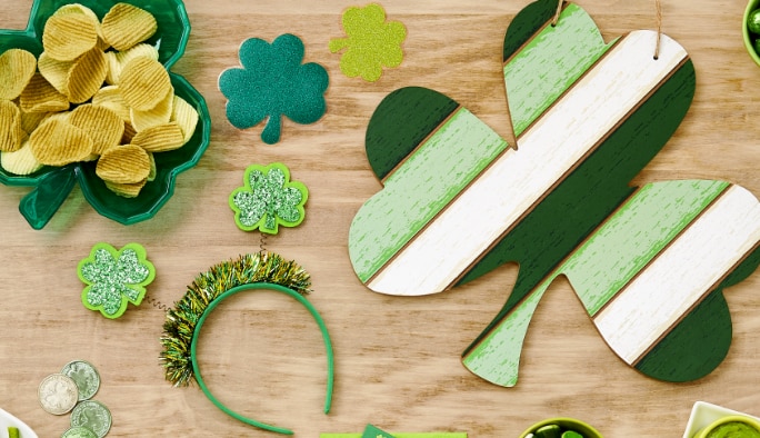 A shamrock-shaped bowl of chips on a table with assorted shamrock-themed party supplies. 