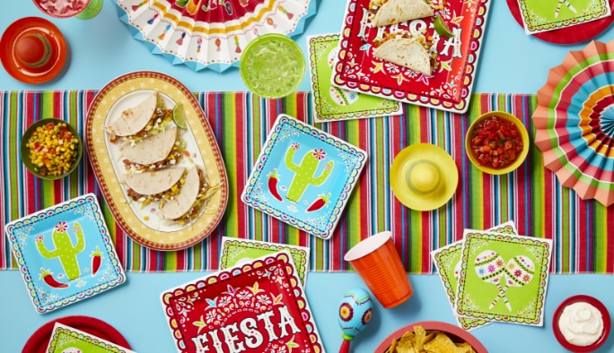 A table filled with tacos and blue, green and red fiesta-themed dinnerware, décor and favours.