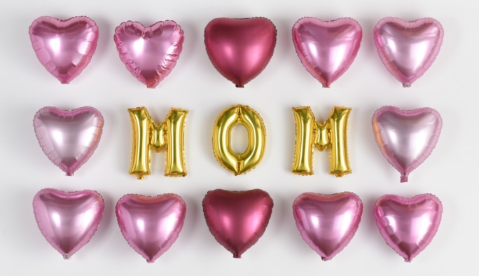 Ballons en aluminium dorés en lettres M-O-M entourés de ballons en aluminium roses en forme de cœurs.