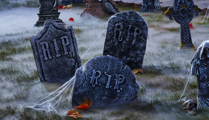 A fog-filled lawn decorated with a variety of Halloween tombstone yard signs and artificial cobwebs.