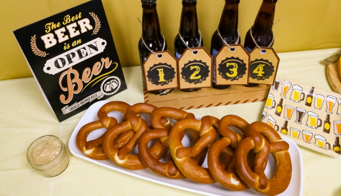 A plate of pretzels and bottles of beer on a table with a variety of beer-themed accessories and napkins.