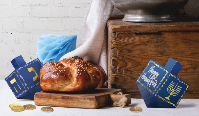 Challah bread and gold gelt coins with large blue and gold 3-D dreidel decorations.