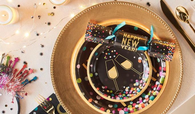 Table avec accessoires noirs, dorés et multicolores avec vaisselle et diablotins à confettis colorés « Happy New Year ».