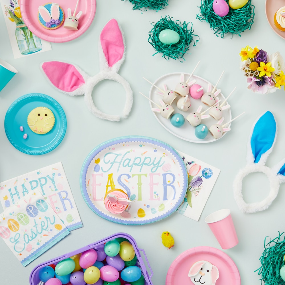 Une surface de table remplie d’accessoires, de friandises et de vaisselle de Pâques, y compris des assiettes ovales de Pâques pastel et des serviettes de table.
