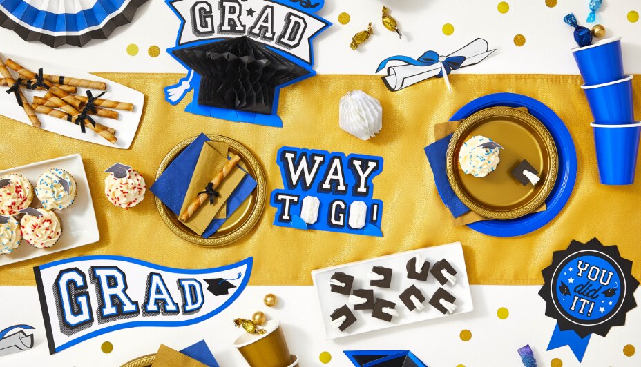 A tabletop filled with blue, white and gold graduation-themed party supplies including a grad room decorating kit.