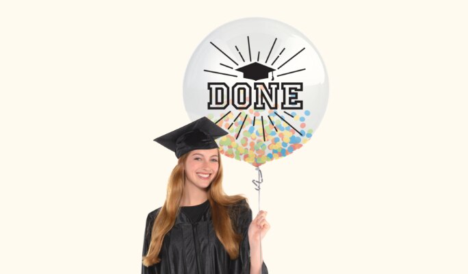 Une femme habillée en robe et mortier tenant un ballon à confettis multicolores à thème de remise des diplômes rempli d’air.