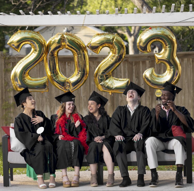 A group of graduates holding themed photo booth props sit in front of large helium-filled gold foil 2-0-2-3 number balloons.
