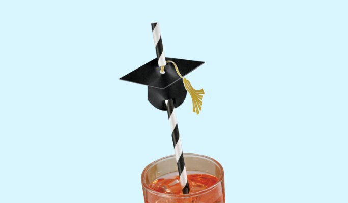A beverage in a glass with a black, white and gold graduation cap straw. 