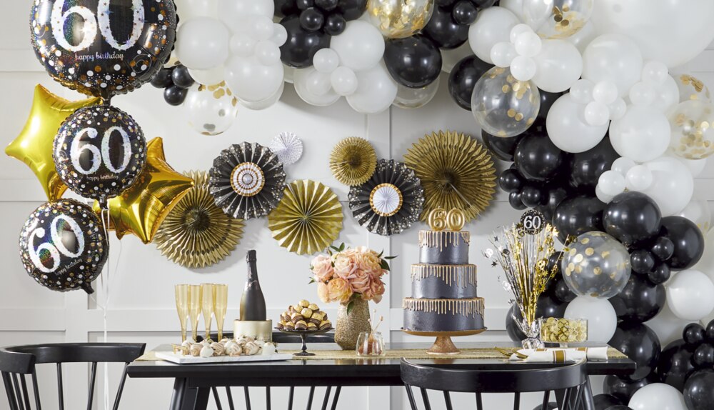 A dining room styled with black and metallic 60th birthday balloons and paper fan decorations.