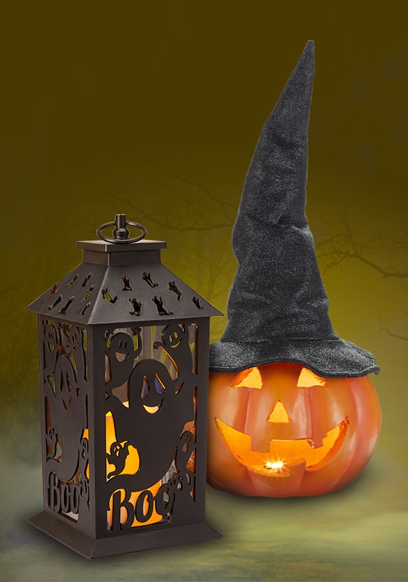 Une lanterne à flamme vacillante à DEL et une citrouille en plastique illuminée à piles portant un chapeau de sorcière.