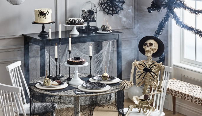 A room styled with black and white Halloween party decor including cobwebs and a prop skeleton.