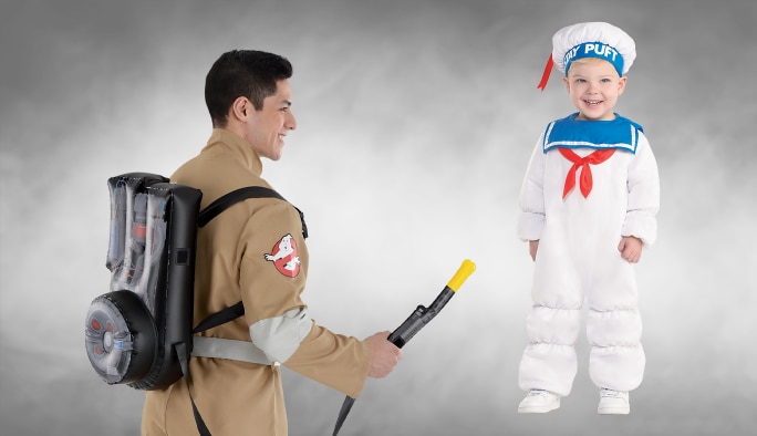 Un homme portant un costume SOS Fantômes avec un pack de protons et un tout-petit portant un costume du Bibendum Chamallow.