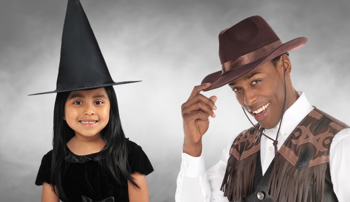 A girl wearing a black witch hat and a man wearing a brown cowboy hat.