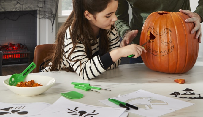 A girl using a various pumpkin decor tools including stencils to decorate a pumpkin.