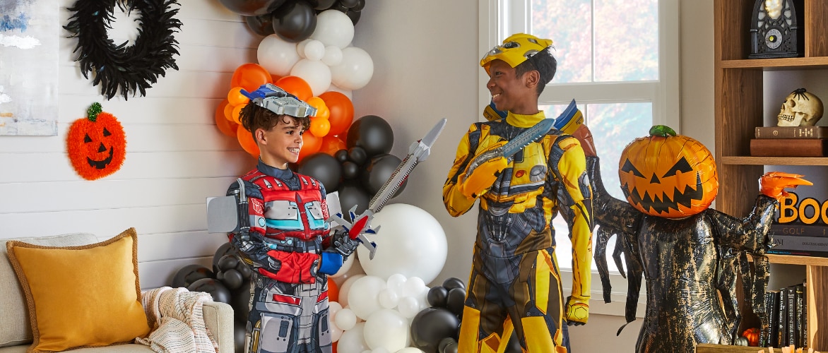Two children wearing Transformers character costumes playing in a room decorated with Halloween balloons. 