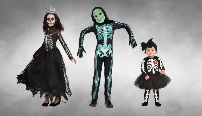 Deux adultes et un bambin portant des costumes et accessoires à thème de squelette.