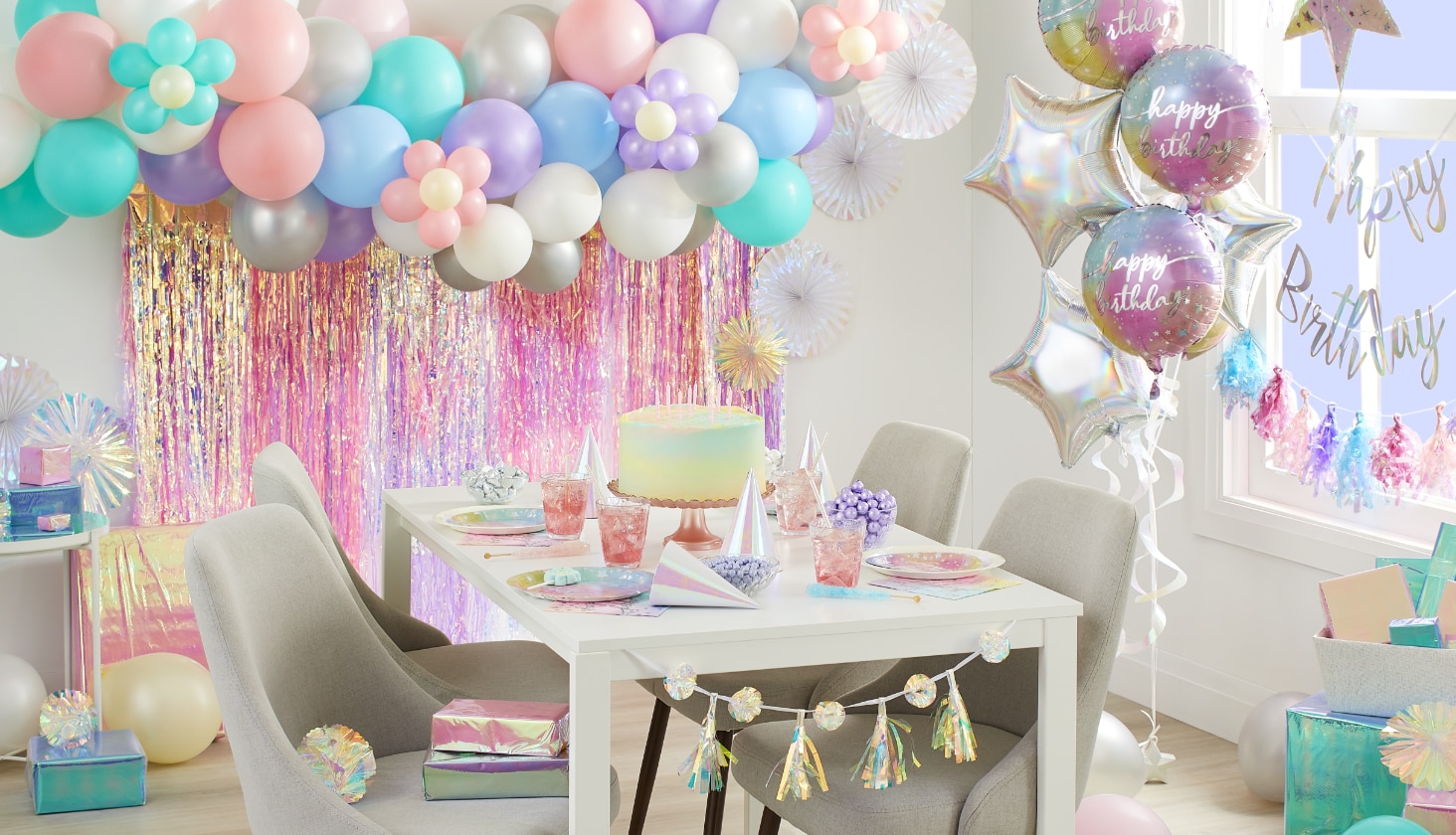 A dining room styled with a balloon arch and a variety of iridescent birthday decorations.