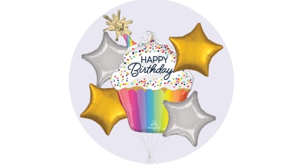 Un ballon en forme de petit gâteau blanc et arc-en-ciel avec les mots « Happy Birthday » sur le devant et entouré de ballons dorés et argentés en forme d’étoiles.