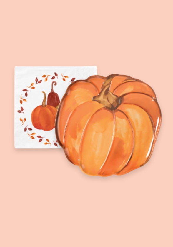 A pumpkin shaped reusable plastic serving platter and a pumpkin and leaves paper napkin.