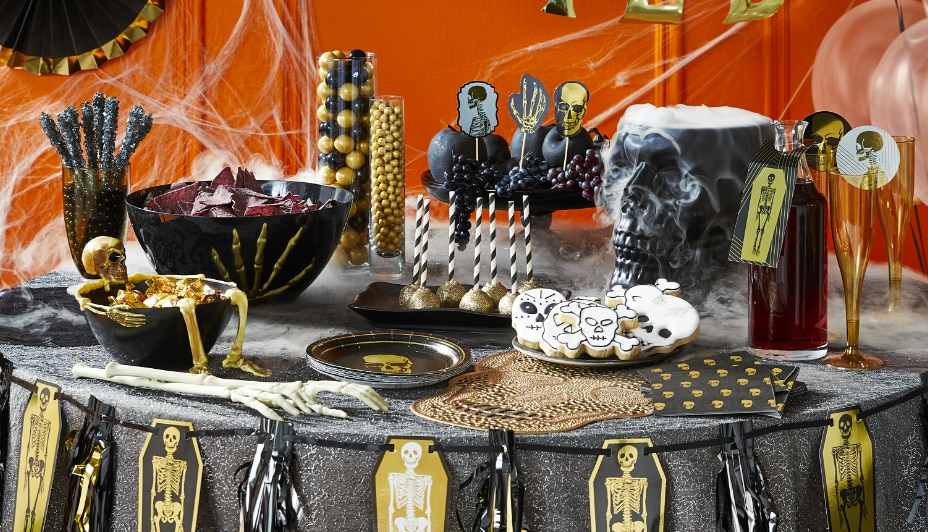 Une table à collations décorée de vaisselle noire et dorée à thème de squelette.