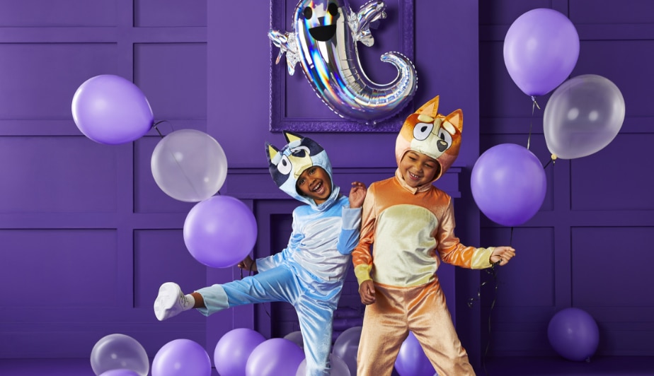 Deux enfants portant des costumes Bluey et Bingo dans une pièce remplie de ballons en latex violets et d’un ballon en aluminium en forme de fantôme.