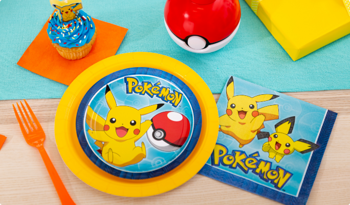 A round Pokémon Pikachu paper plate, a napkin and various colourful party supplies on a table.