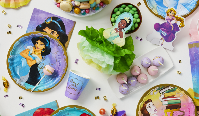 Articles de fête à thème des Princesses Disney Jasmin, Tiana et Raiponce et des friandises sur une table.