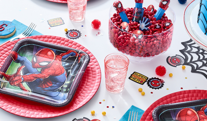 A Marvel Spider-Man paper plate and various themed supplies and candies on a table.