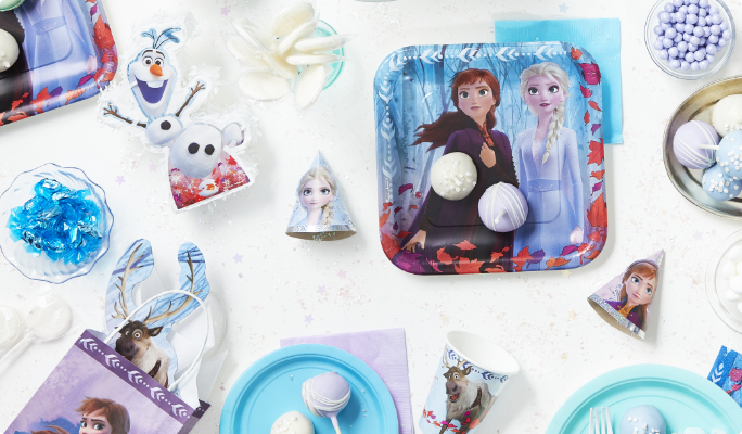 A Frozen 2 favour cup and square plate on a table with various themed supplies and candies.