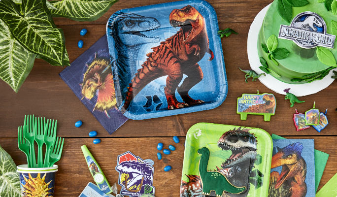 Various Jurassic World square paper plates, party favours, a cake and candy on a table.