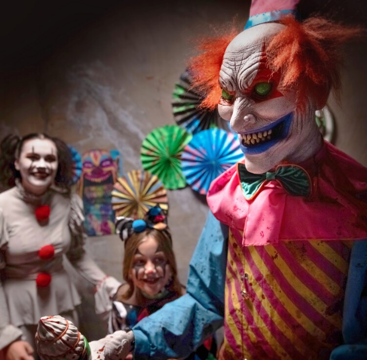 A woman, a girl and a man wearing scary clown costumes in a room decorated with creepy carnival Halloween decor.